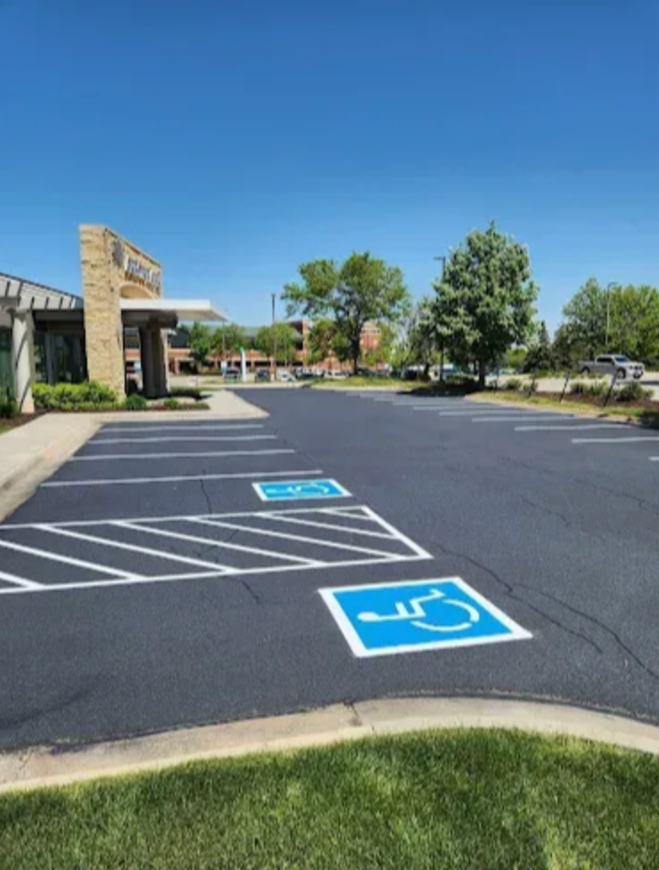 Two blue and white accessible parking spaces with a marked access aisle in a paved lot next to a building entrance.