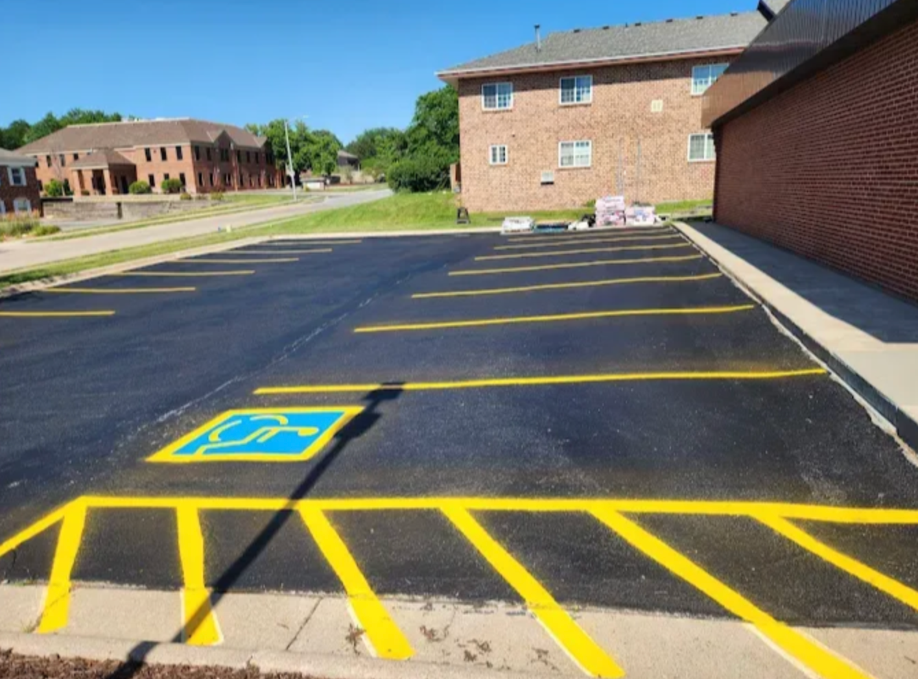 A freshly paved parking lot featuring a blue and yellow ADA handicap accessible parking space with yellow striped aisles.