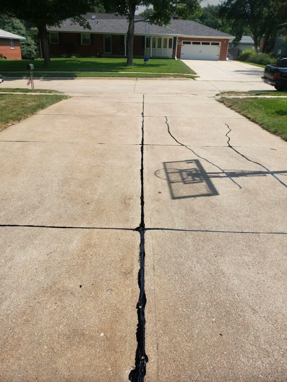 A concrete driveway with a large center crack filled with dark sealant and another diagonal crack to the right.