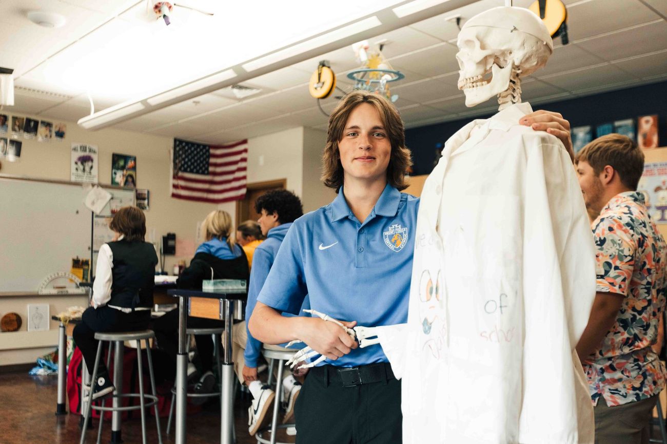 A young man is standing next to a skeleton in a classroom.