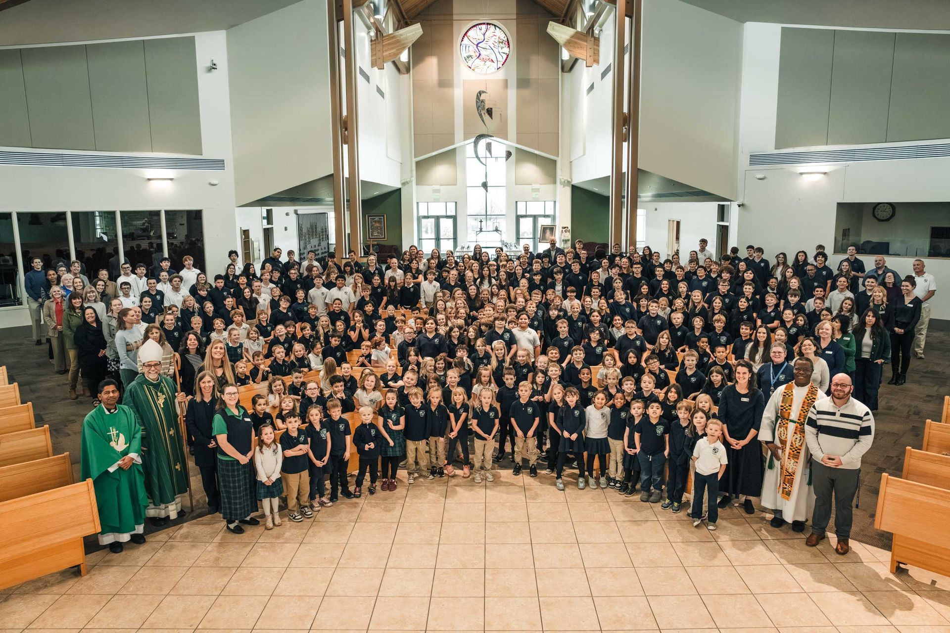 Group of people in a church, posing for a photo. Many children and adults, inside a bright building with pews.