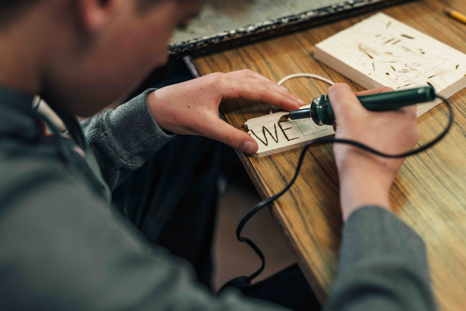 A man is using a soldering iron to write on a piece of wood.