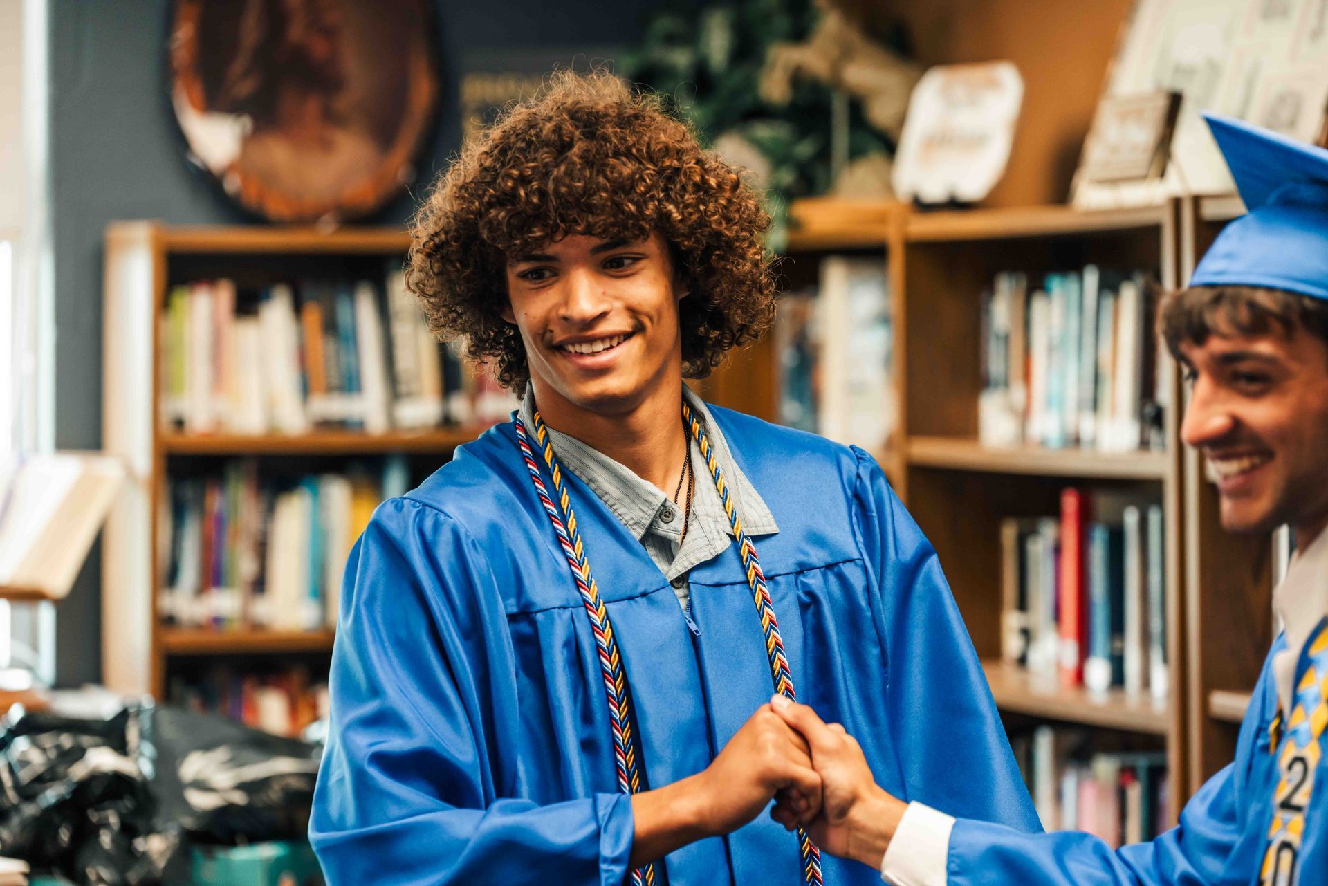 Two graduates are shaking hands in a library.