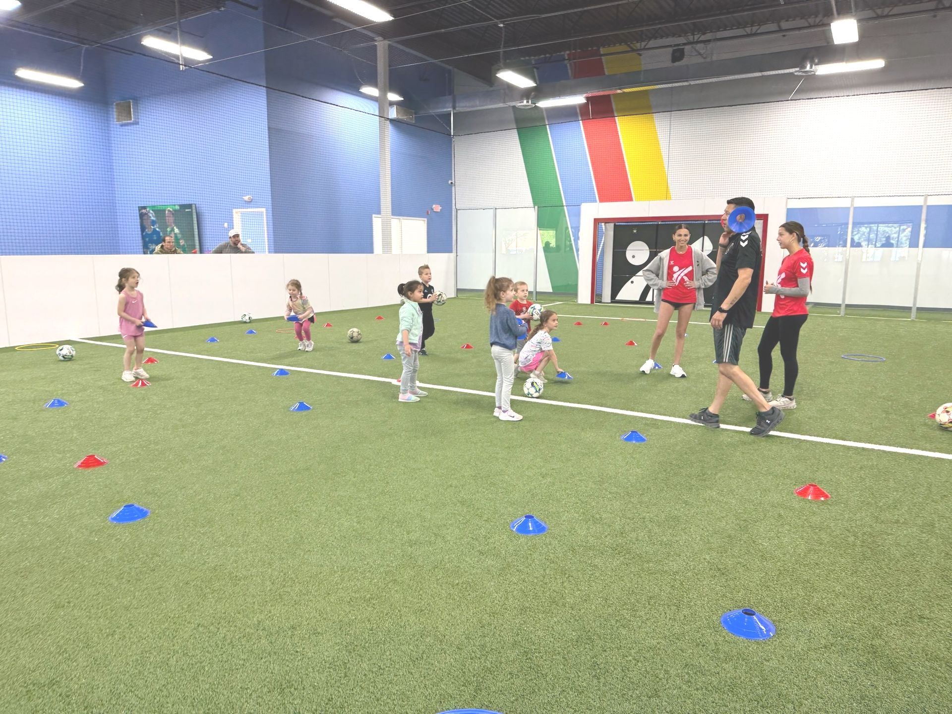 A group of children are playing soccer on a indoor field.