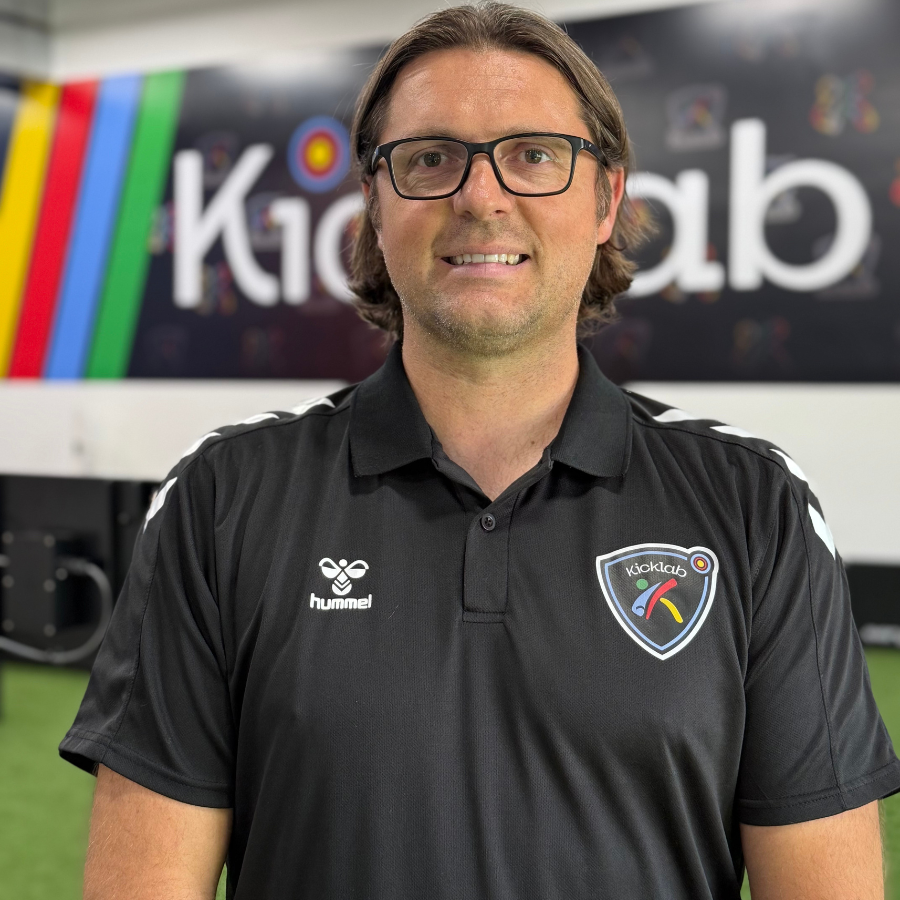 Man in black polo shirt with glasses smiles at the camera. Behind him is the 