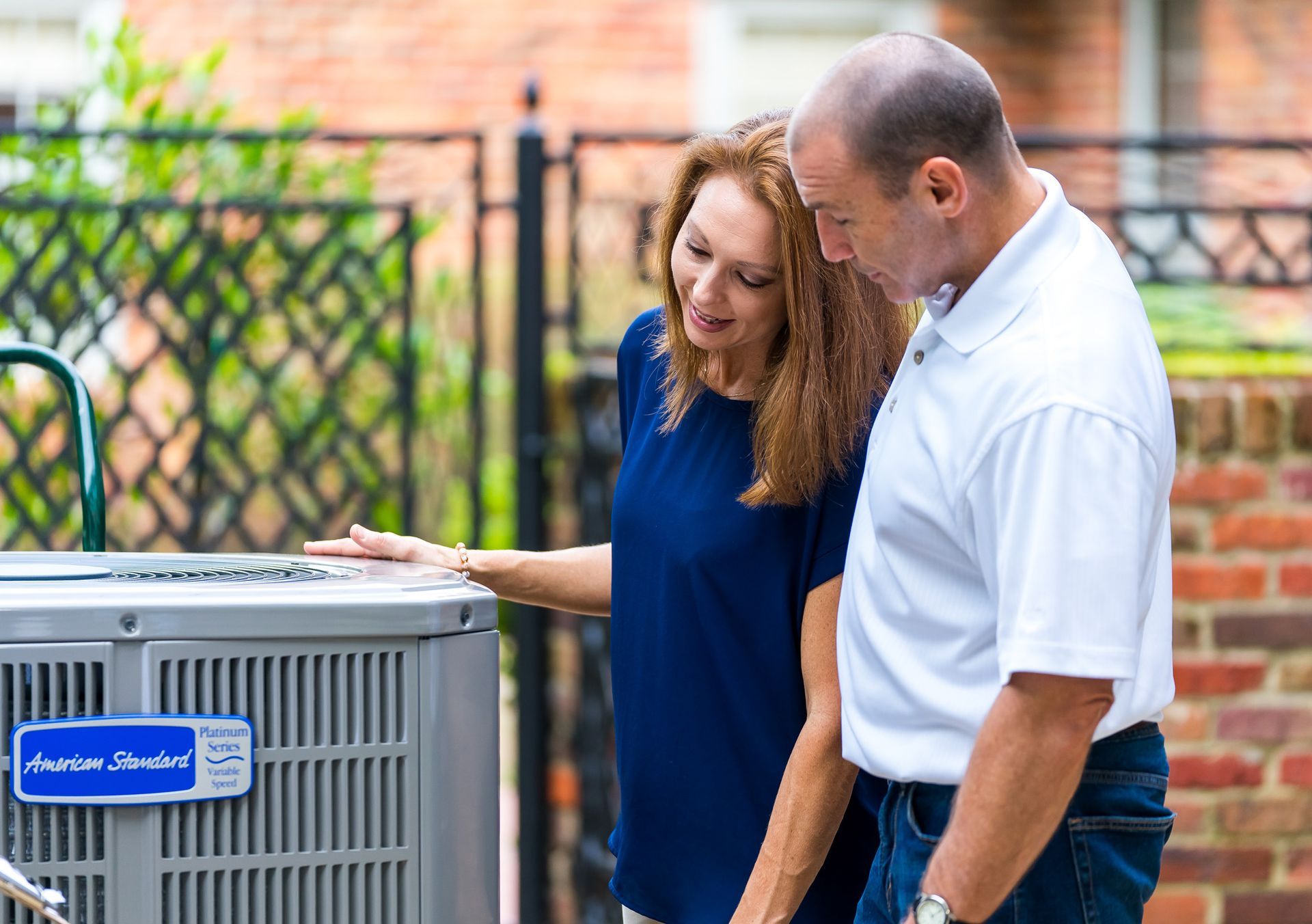Couple looking at an air conditioning unit outside, with the woman pointing to it.