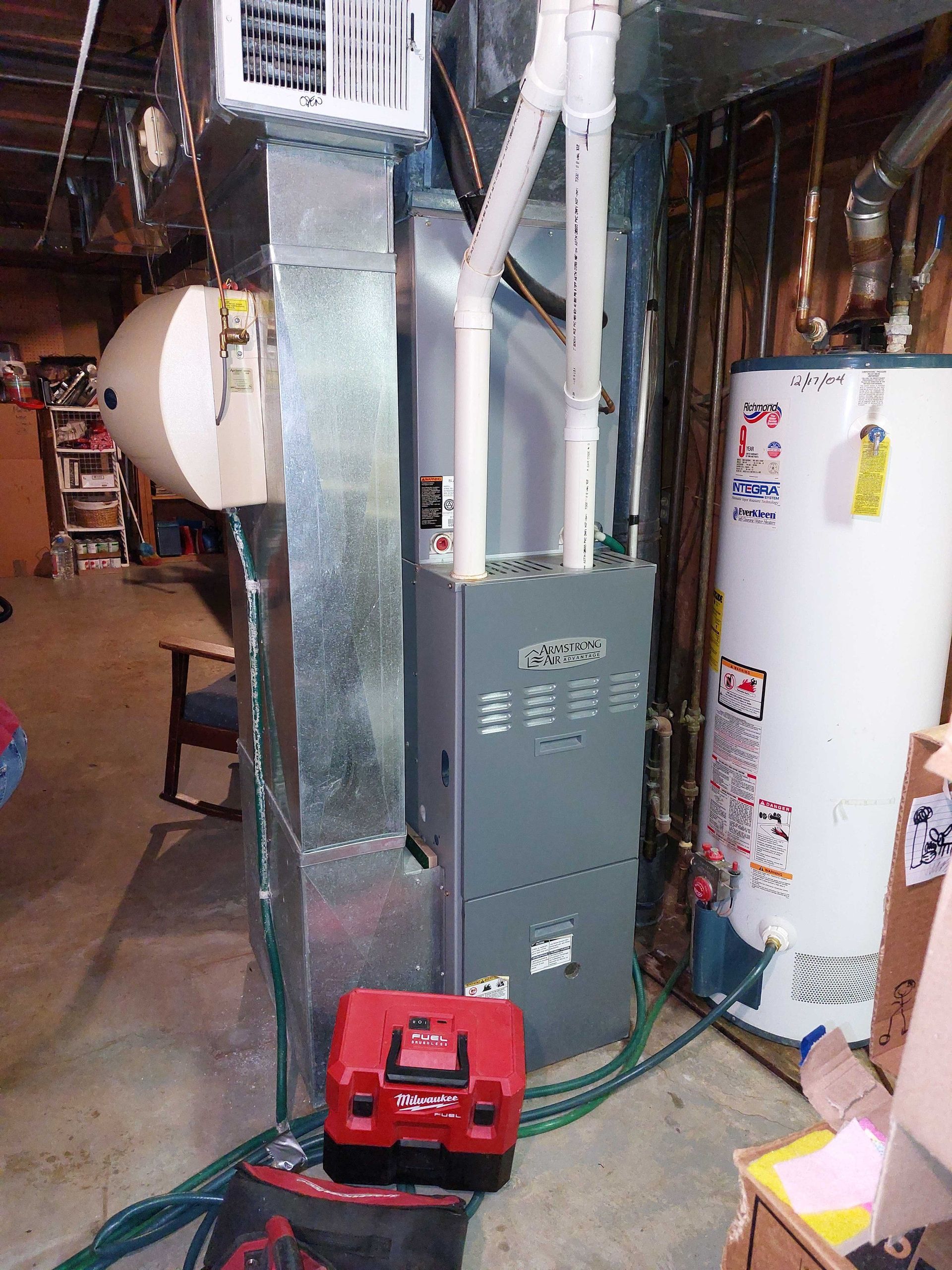 Furnace and water heater in a basement with ductwork and a red vacuum.
