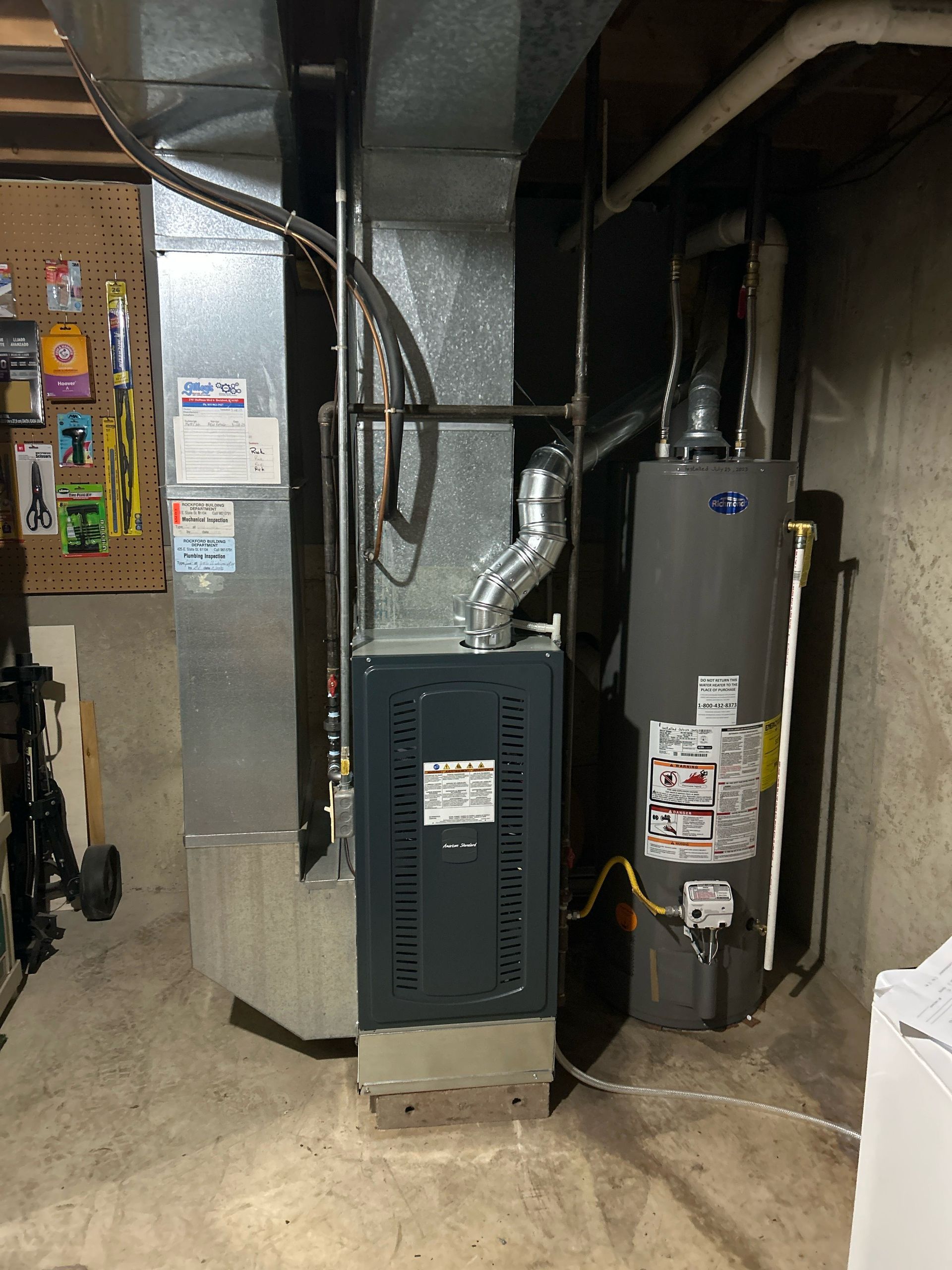 Furnace and water heater in a basement. The furnace is gray, next to a gray water heater.