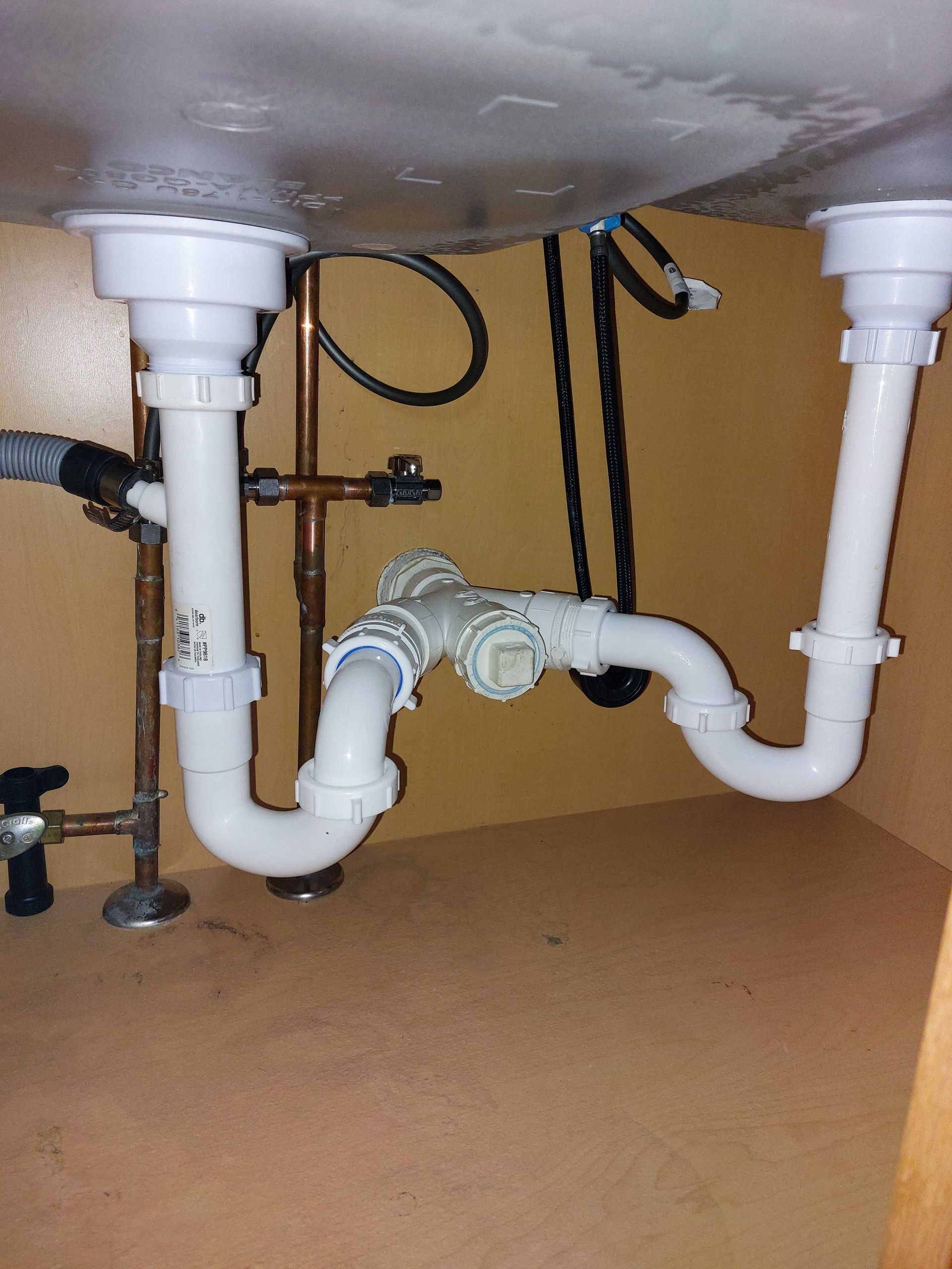 Under-sink plumbing with white pipes, including P-traps, connecting two drains to a central drain pipe.