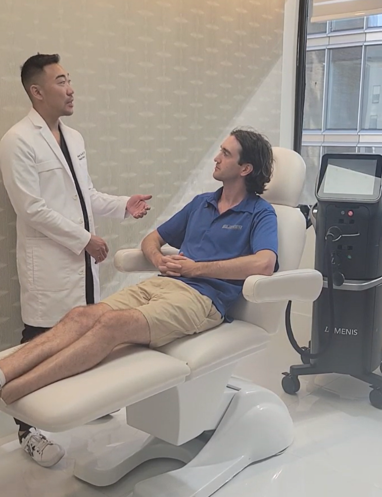A doctor in a white coat consults with a patient sitting in a medical chair, clinic setting.