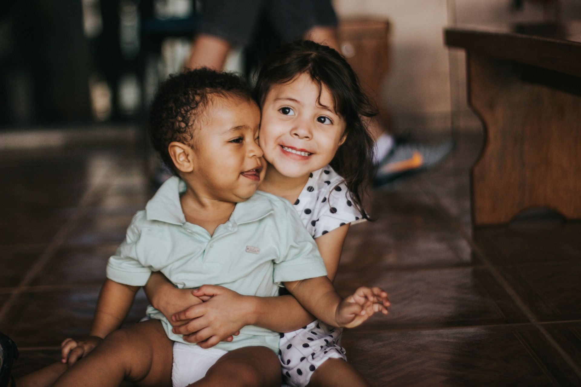 A boy and a girl are sitting on the floor hugging each other.