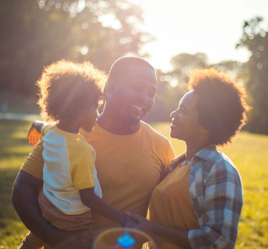 A man and woman are holding a child in their arms in a park.