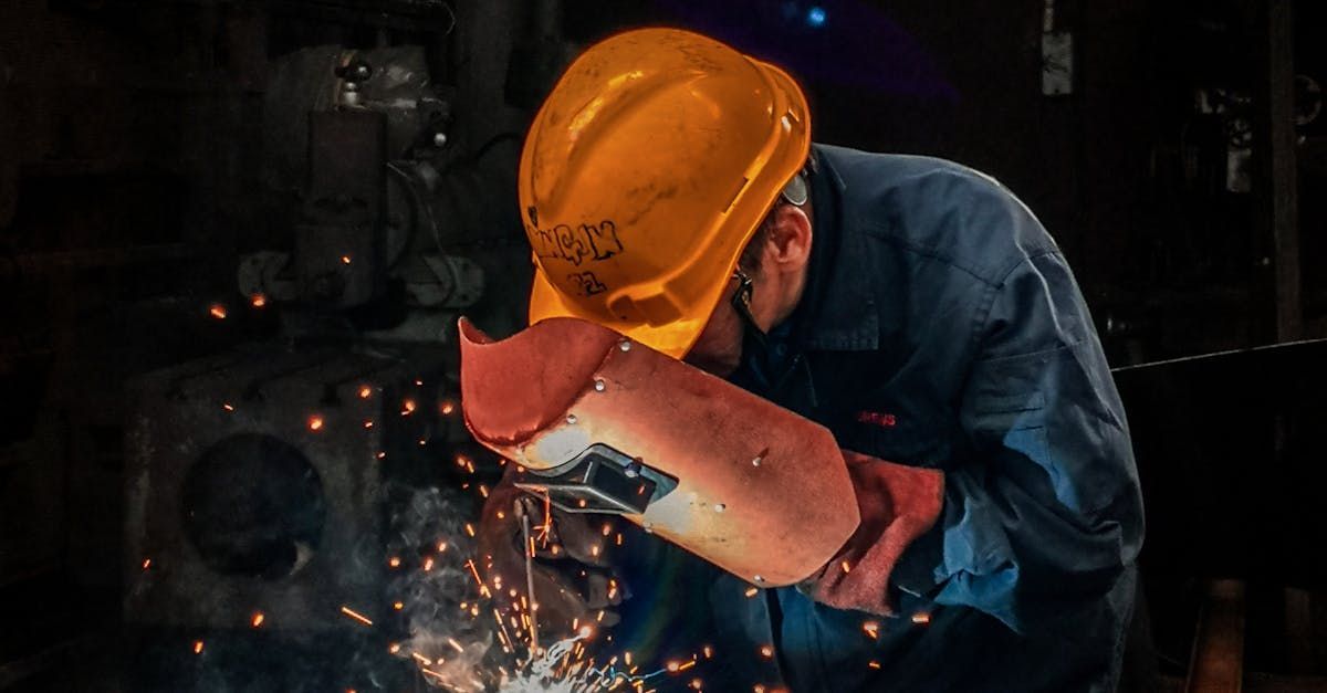 A man wearing a hard hat and gloves is welding a piece of metal.