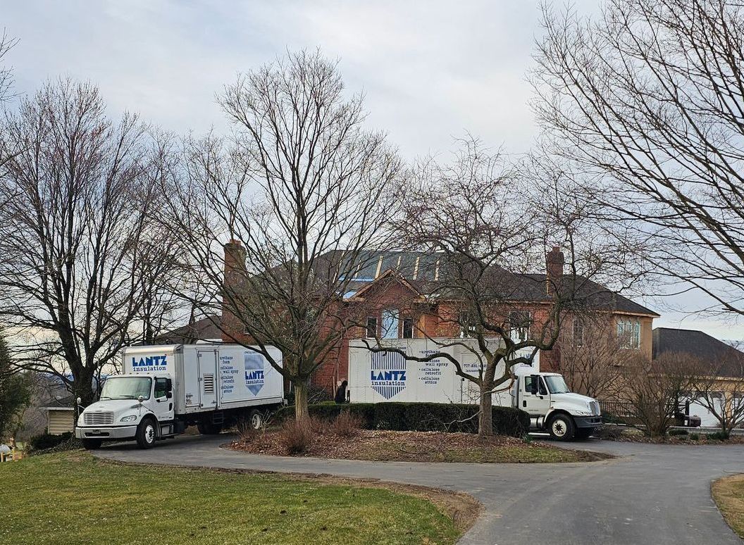 Two moving trucks are parked in front of a brick house.