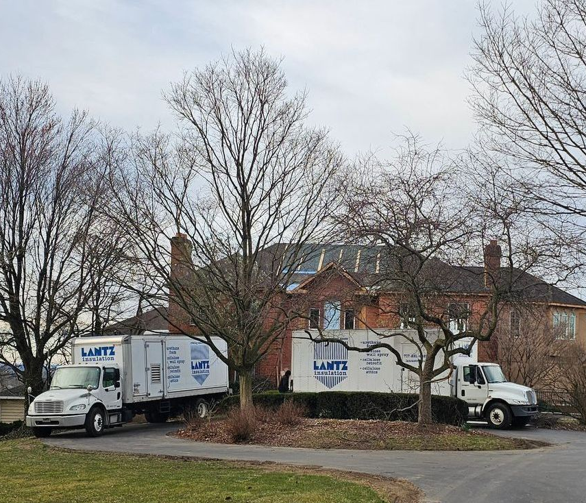 Two moving trucks are parked in front of a brick house.