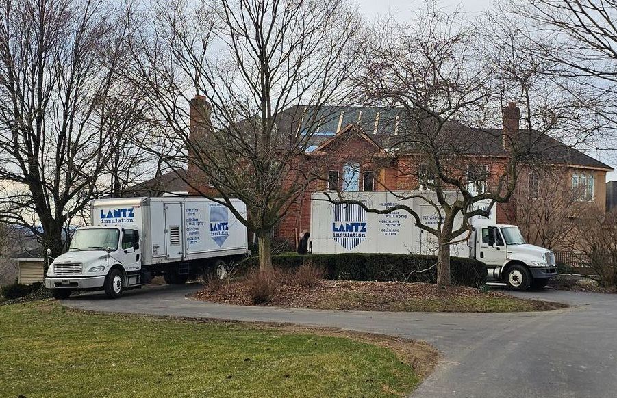 Two insulation trucks are parked in front of a house.