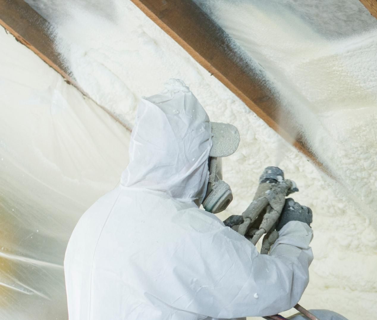 A man is spraying insulation on the ceiling of a building.