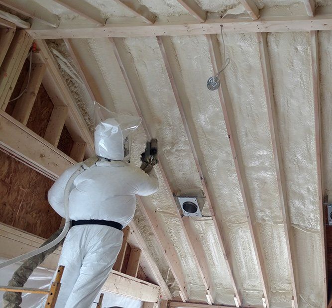 A man is spraying foam on the ceiling of a building.