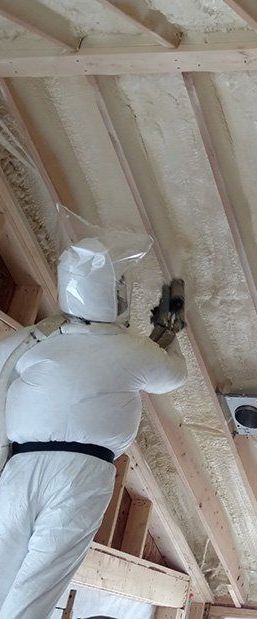 A man is spraying foam on the ceiling of a building.