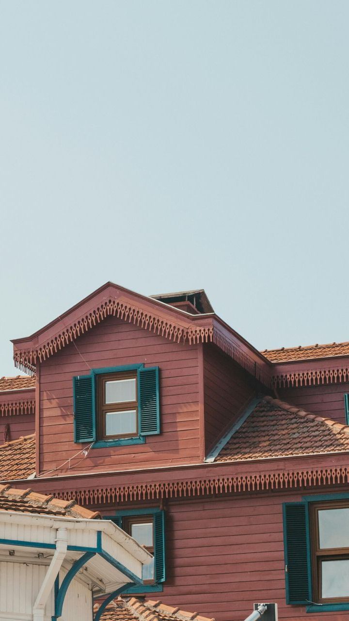 The roof of a red brick house with green shutters and a blue sky in the background.