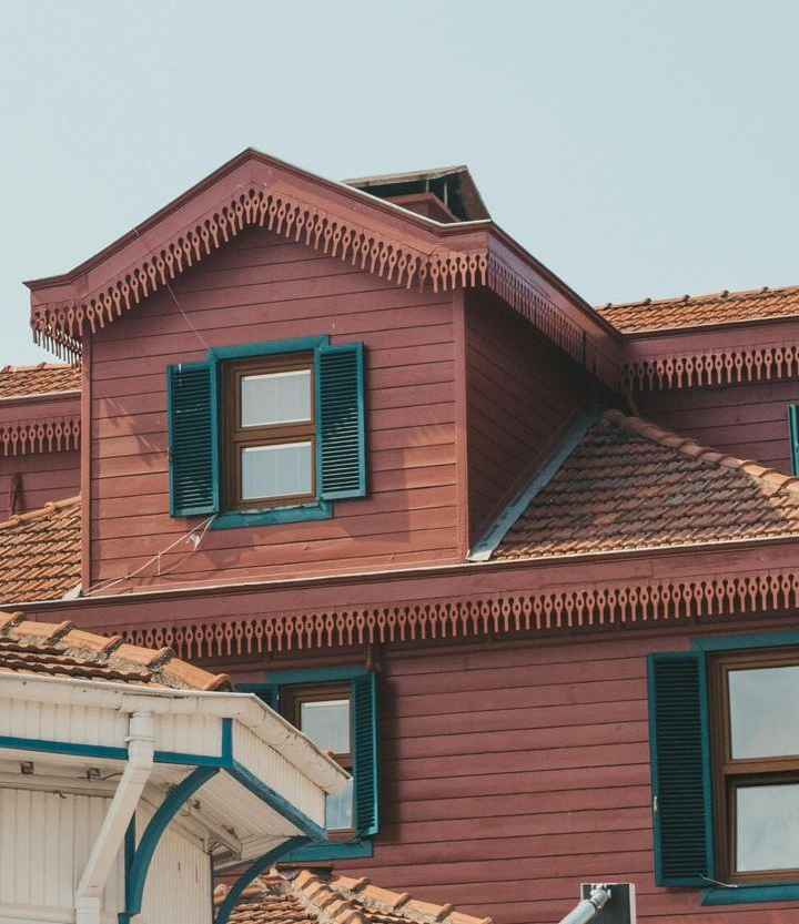 The roof of a red brick house with green shutters and a blue sky in the background.