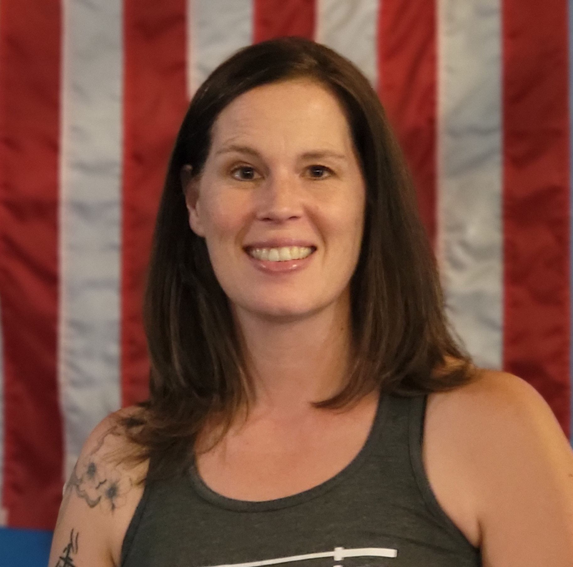 Woman smiling, wearing a gray tank top, with an American flag background.