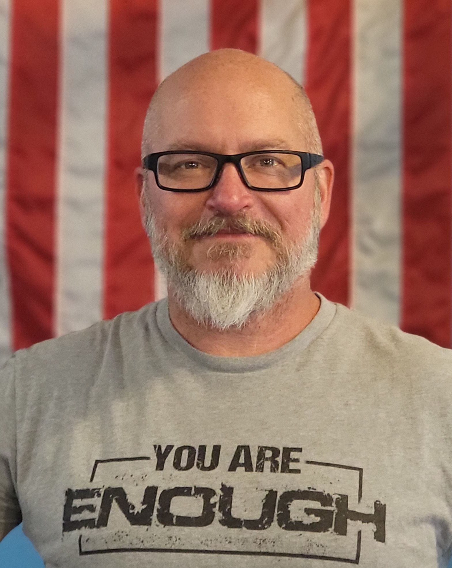 Man with glasses and beard wearing a grey t-shirt with 
