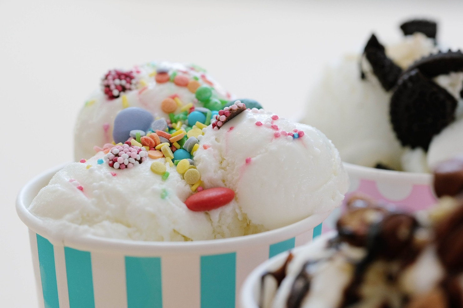 Three cups of ice cream with sprinkles and chocolate on a table.