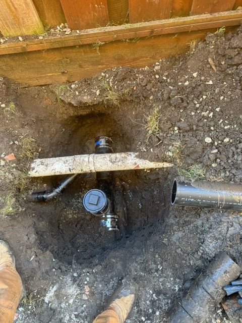 A pipe is being installed in a hole in the ground next to a wooden fence.