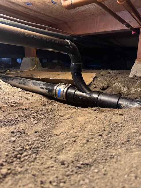 A pipe is laying in the dirt under a house.