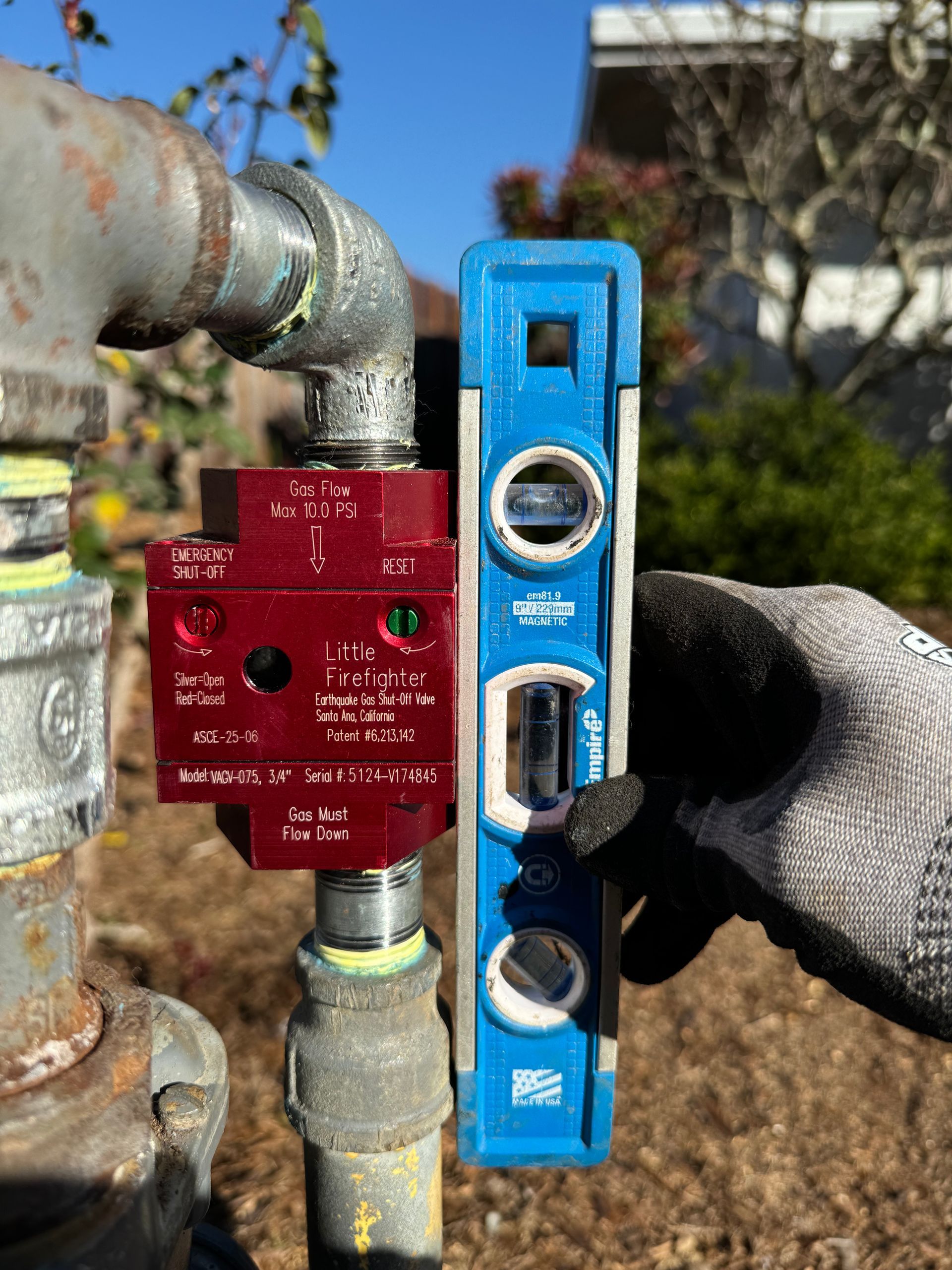 A person is holding a blue level next to a pipe.