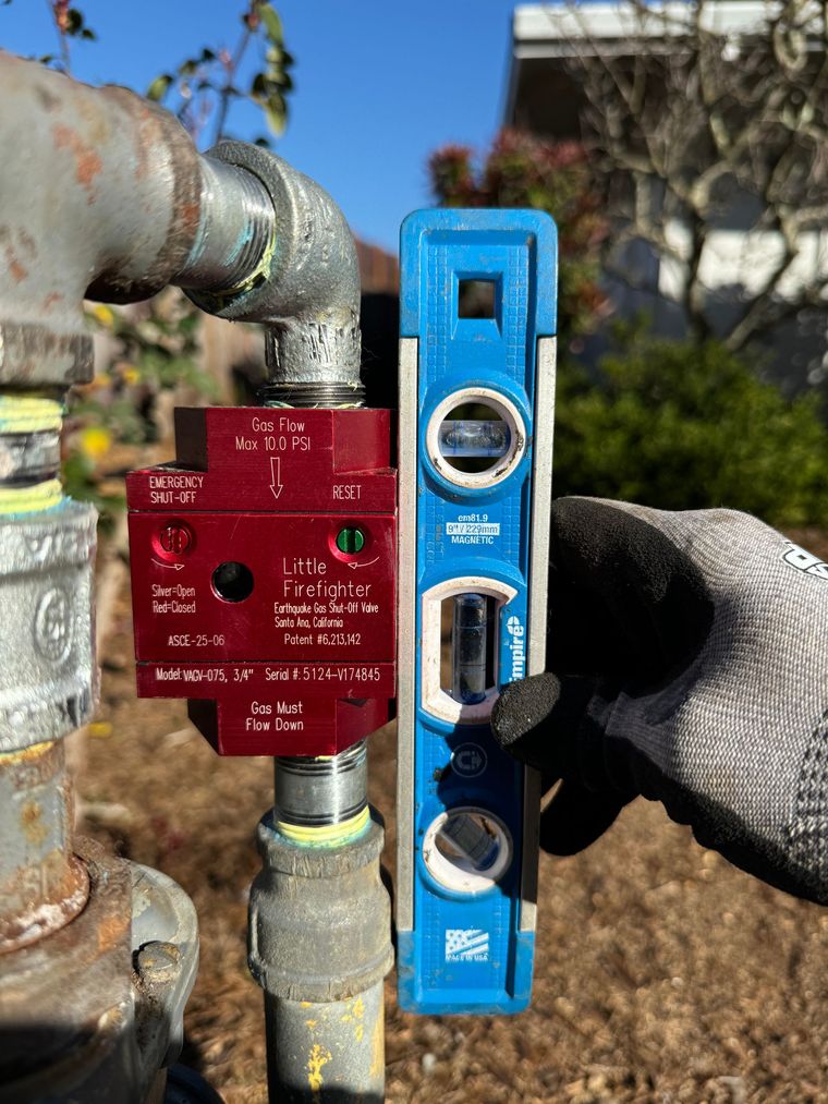 A person is holding a blue level next to a pipe.