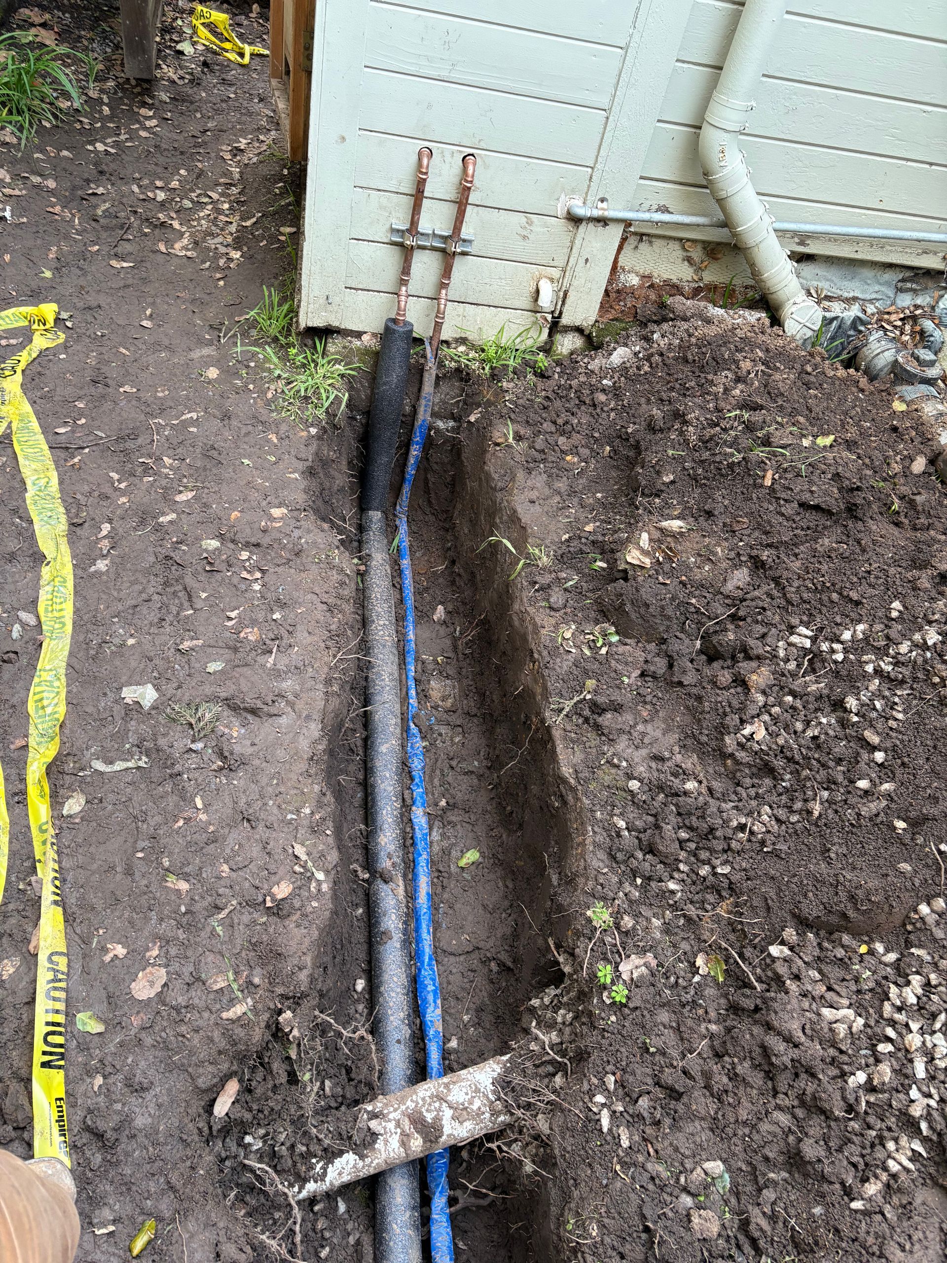 A pipe is being installed in the ground next to a house.