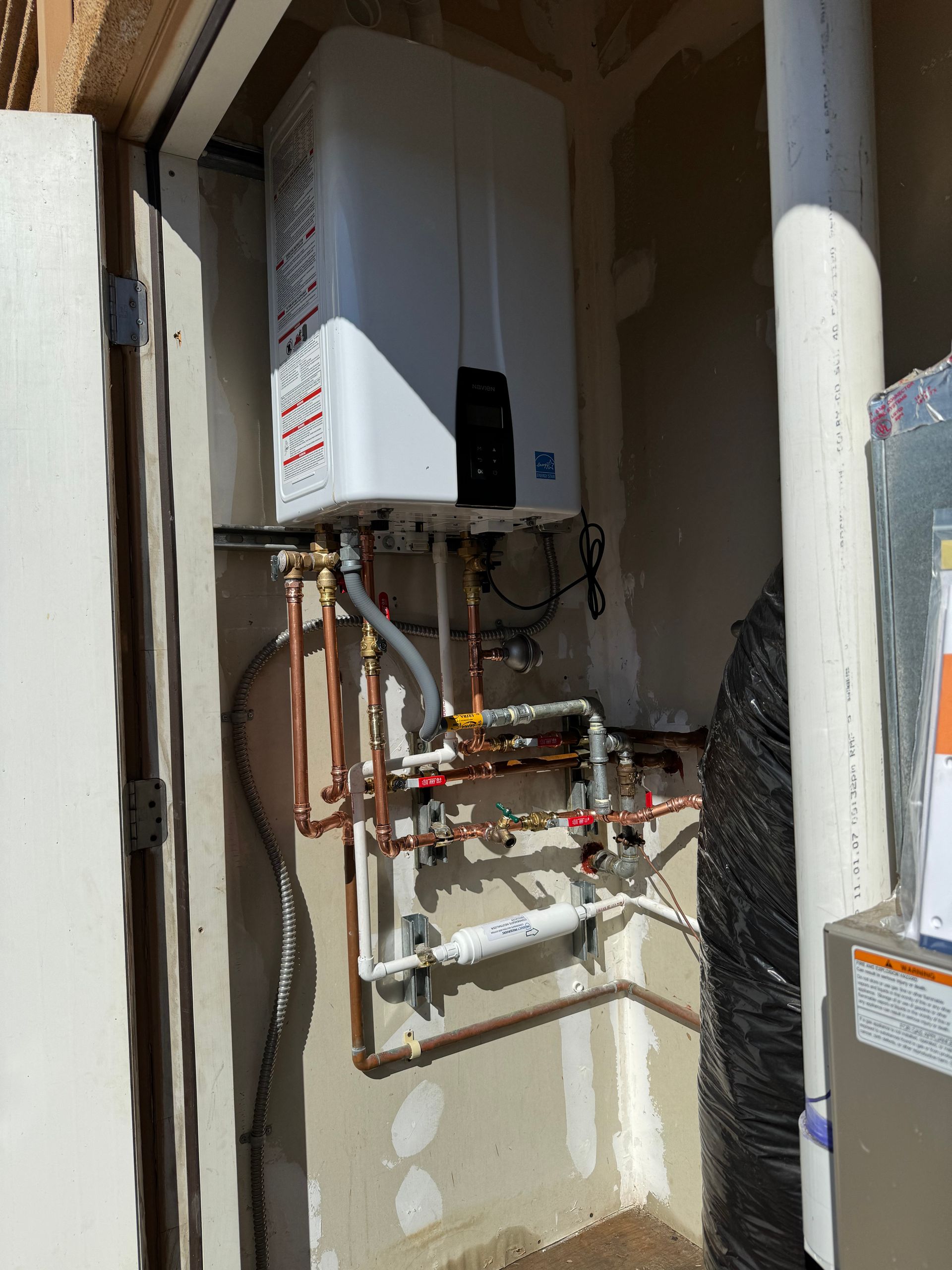 A white water heater is sitting on a wall next to copper pipes.
