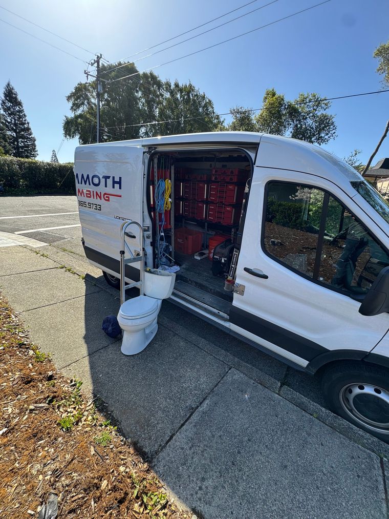 A white van with a toilet in the back is parked on the side of the road.