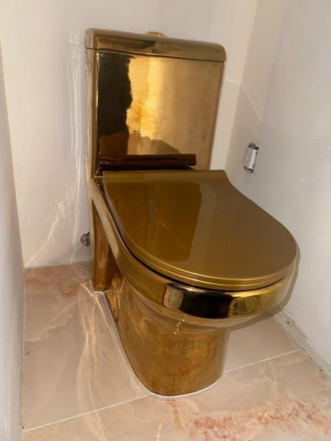 A gold toilet is sitting on a tiled floor in a bathroom.