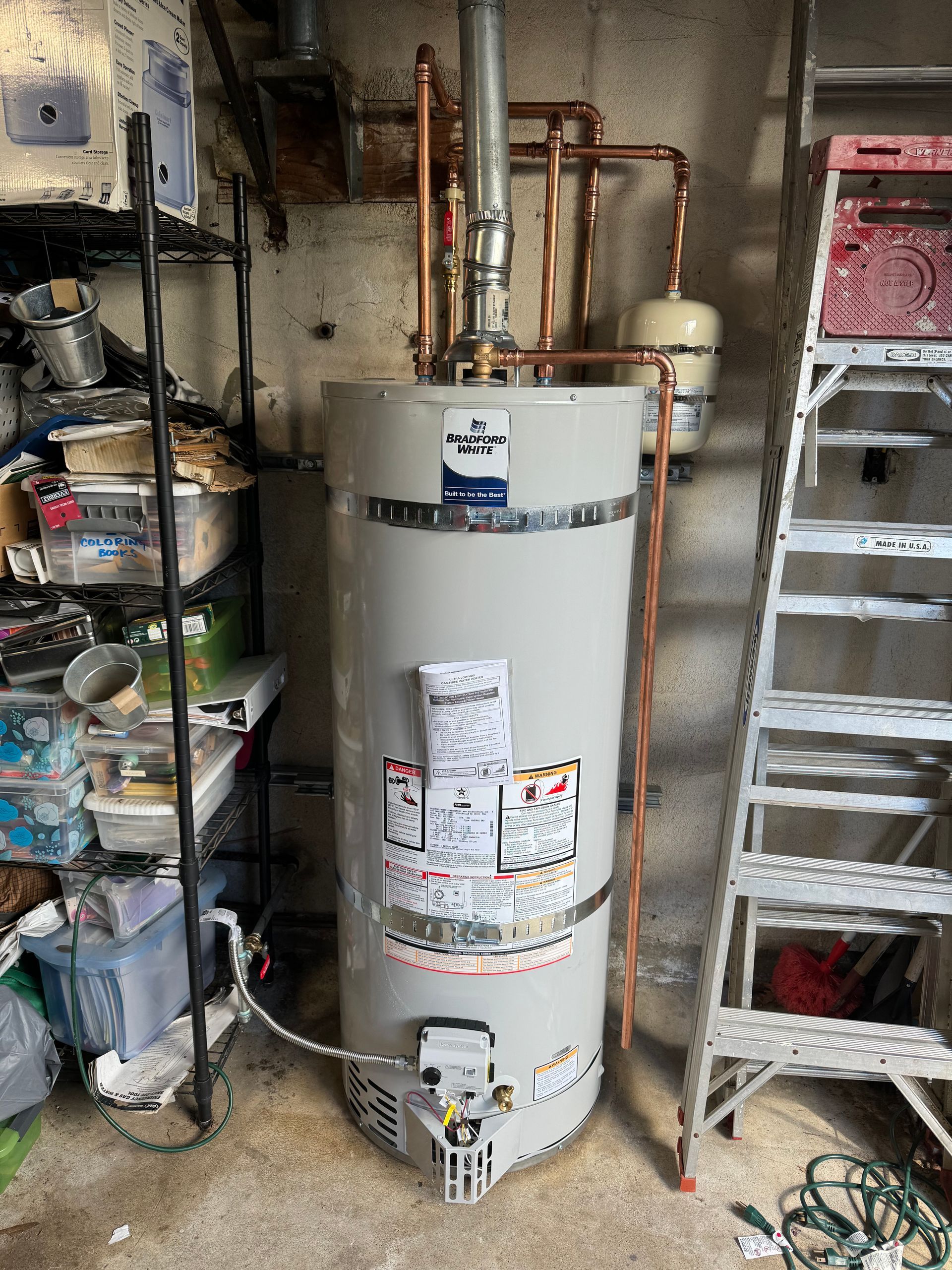 A water heater is sitting in a garage next to a ladder.
