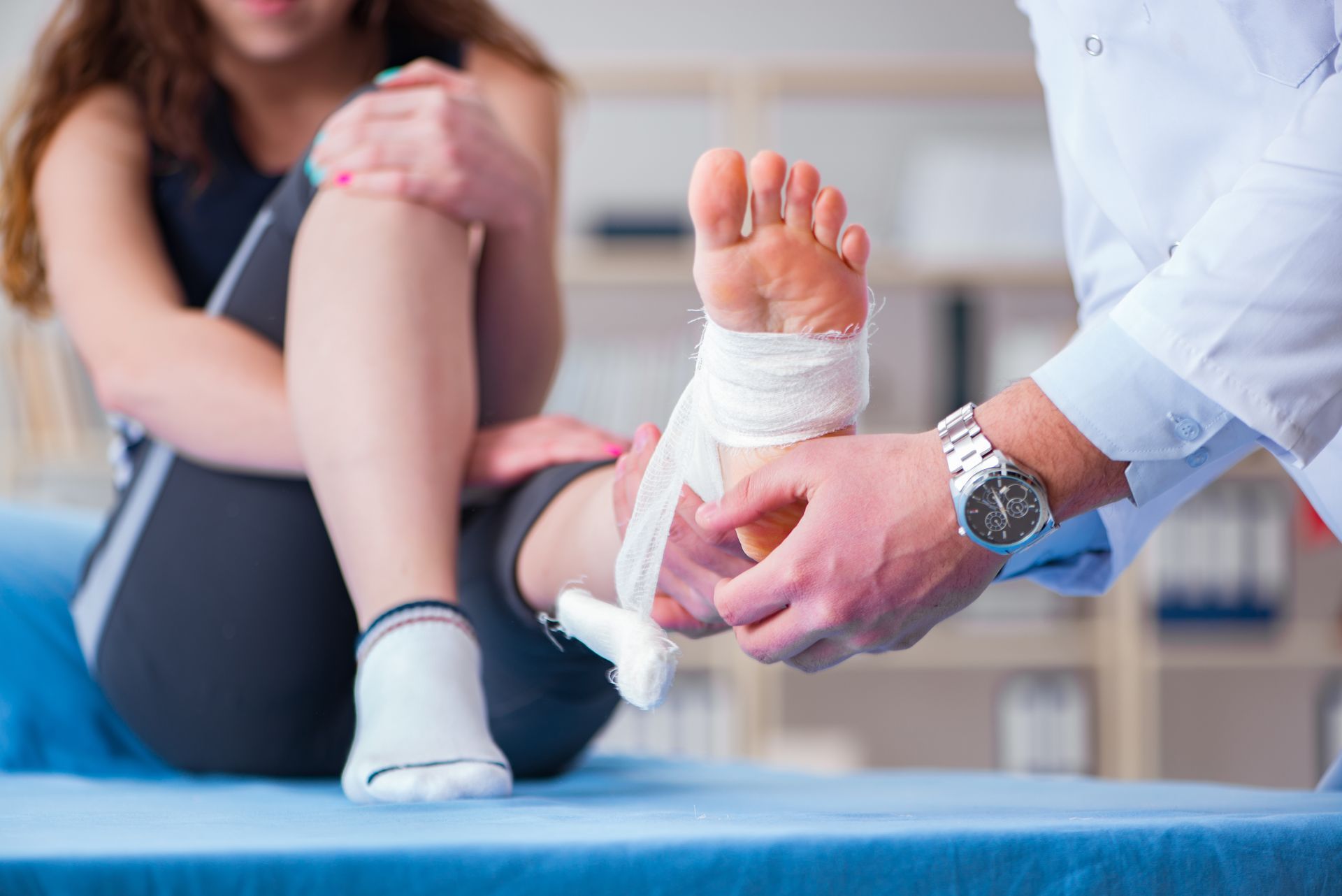 Sports injury doctor wrapping ankle bandage for athlete with foot injury on exam table.