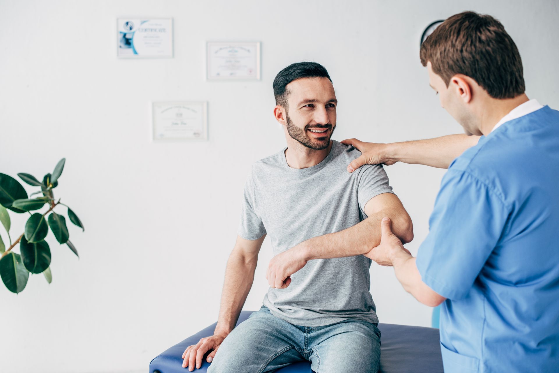 Smiling patient sitting on couch and doctor examining patient shoulder.