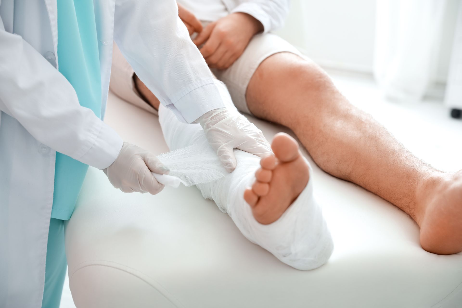A doctor covers the leg of a patient in plaster, inside a doctor’s office.