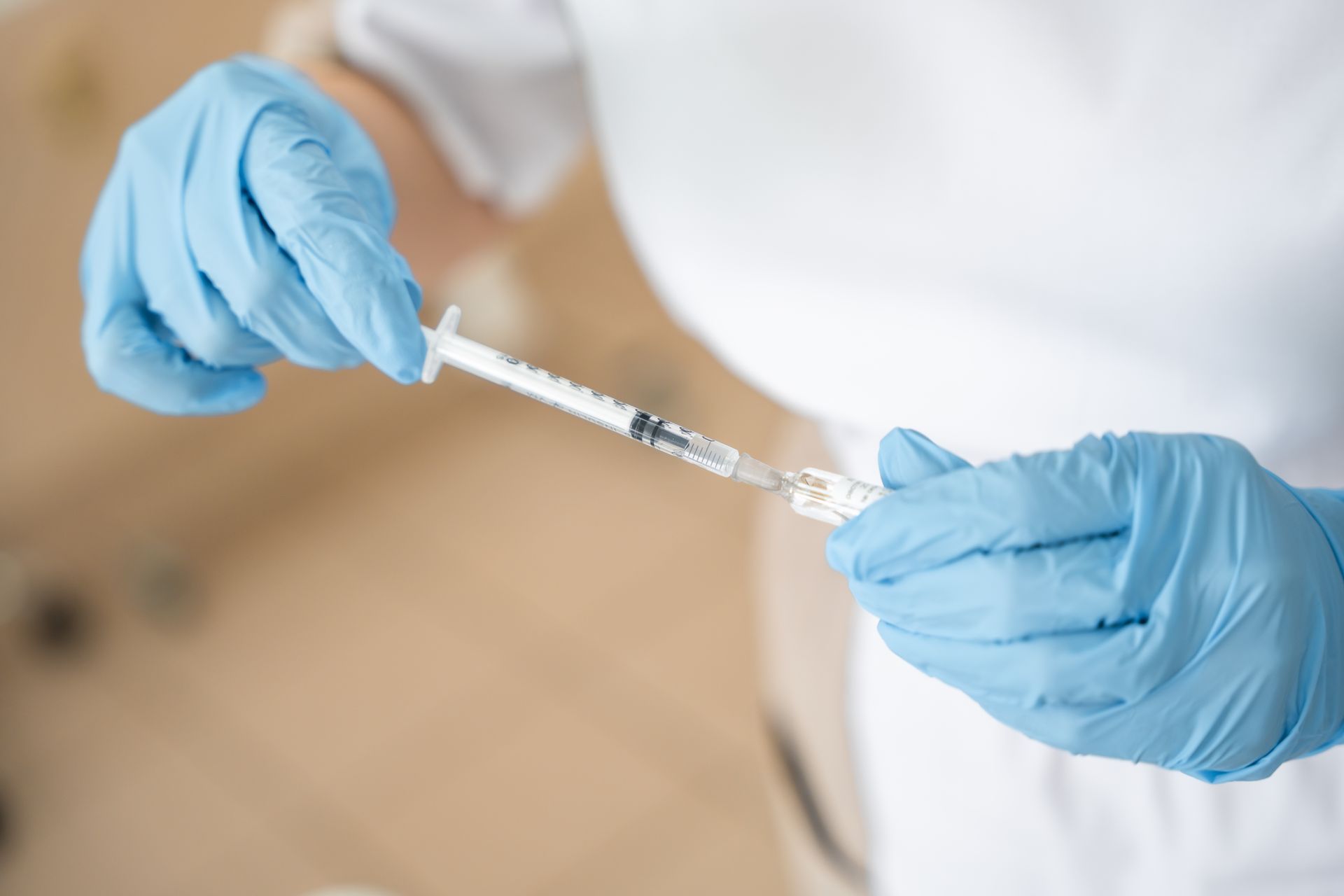 Close-up of a doctor's hand filling a vaccine syringe before injection.