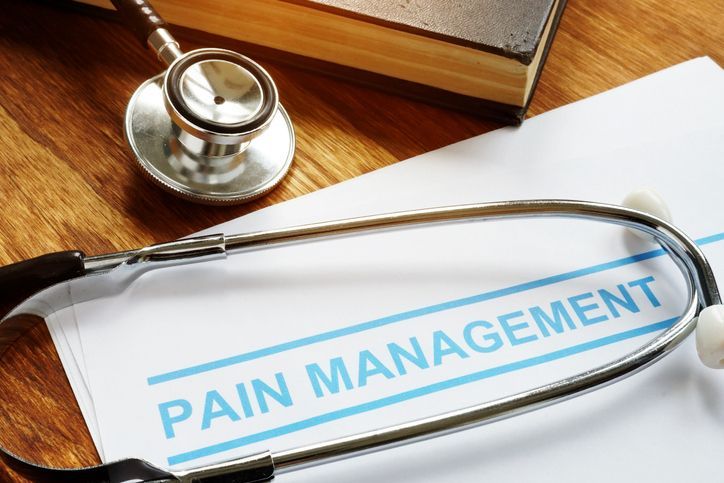 Pain management documents with a stethoscope resting on an open medical reference book.