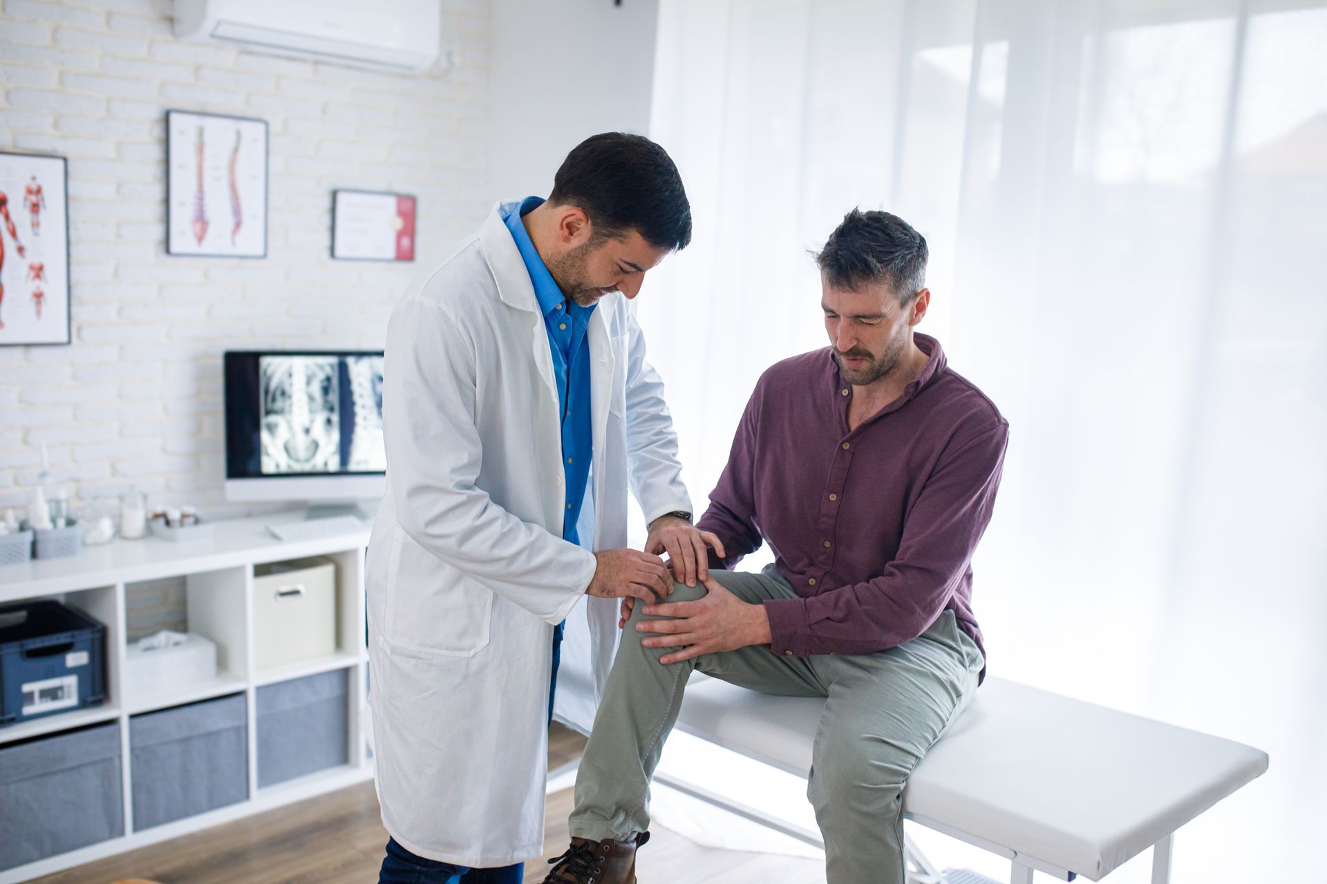 Doctor examining a male patient’s knee, assessing joint pain during an orthopedic clinic visit.