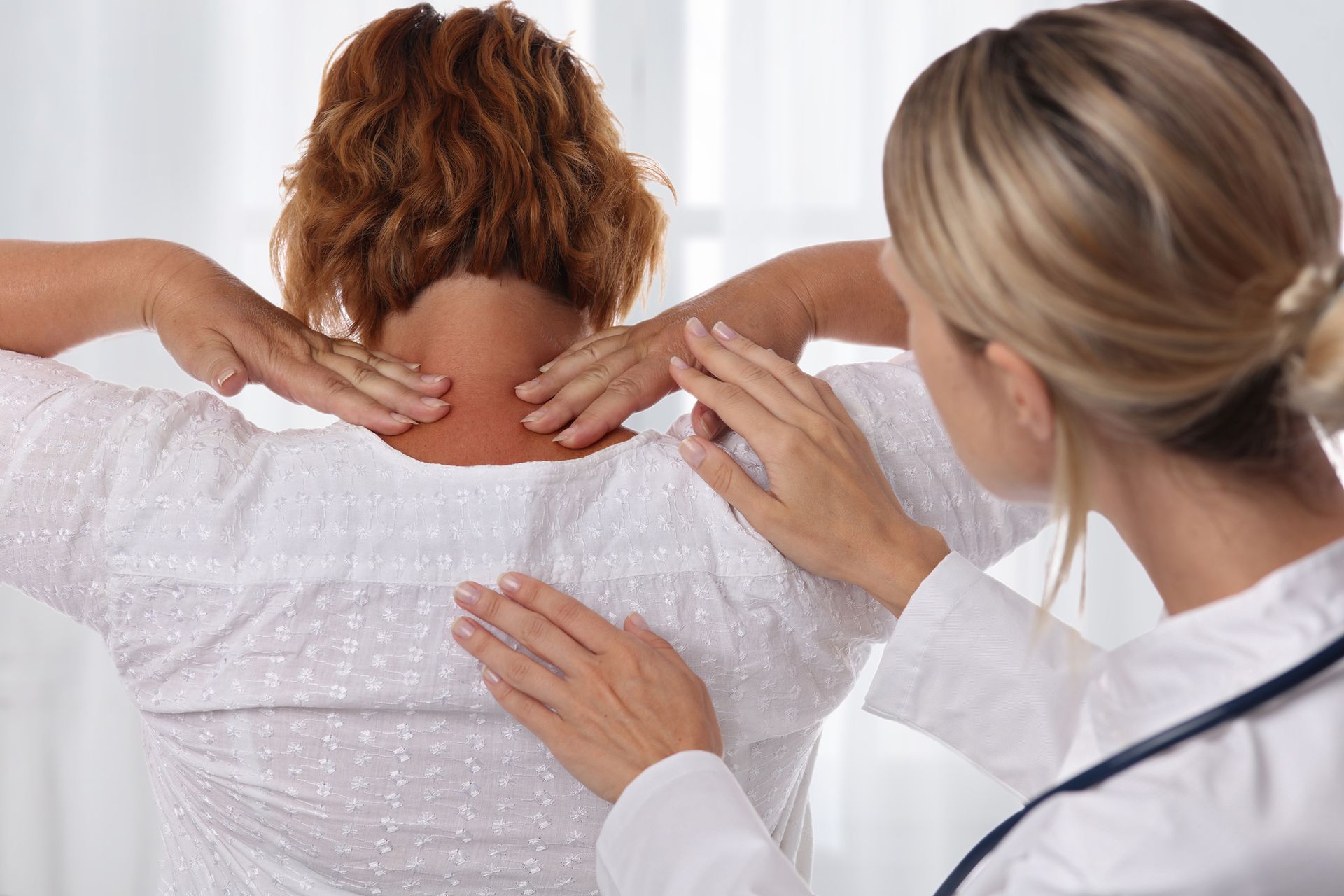 Doctor examining patient's back and neck pain during medical checkup, healthcare consultation.