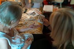 Two women examine a pill organizer. One is older, seated, the other is younger, holding the pills.