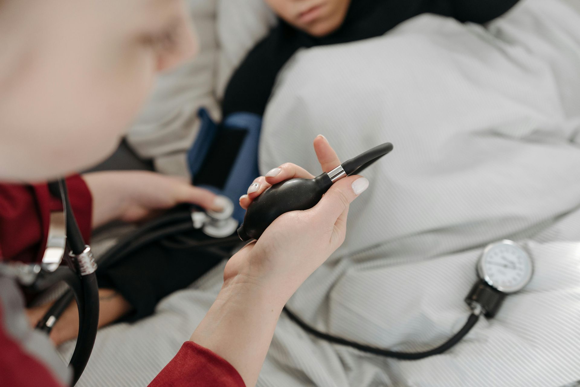 A person's blood pressure is being measured by another person in a bed; medical setting.