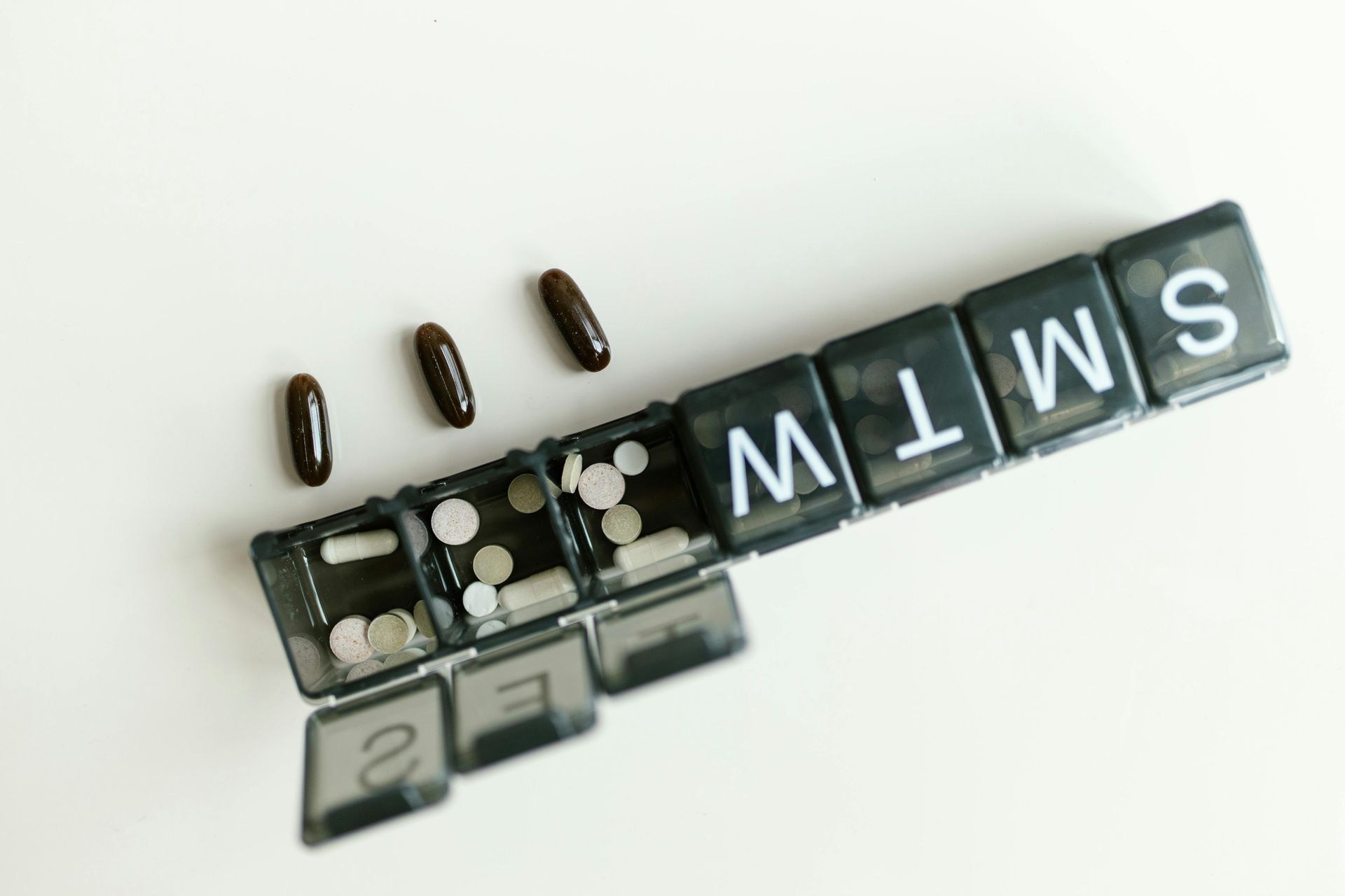 A pill organizer with pills in several compartments, with three pills lying beside it on a white surface.