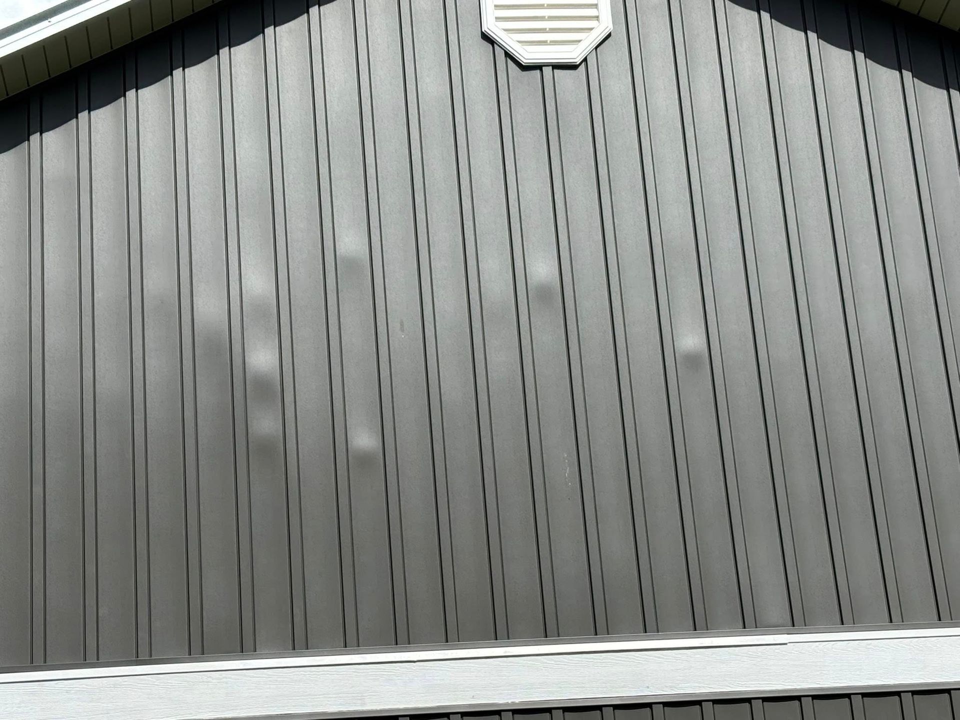 Gray siding on a building with several visible dents or bulges.