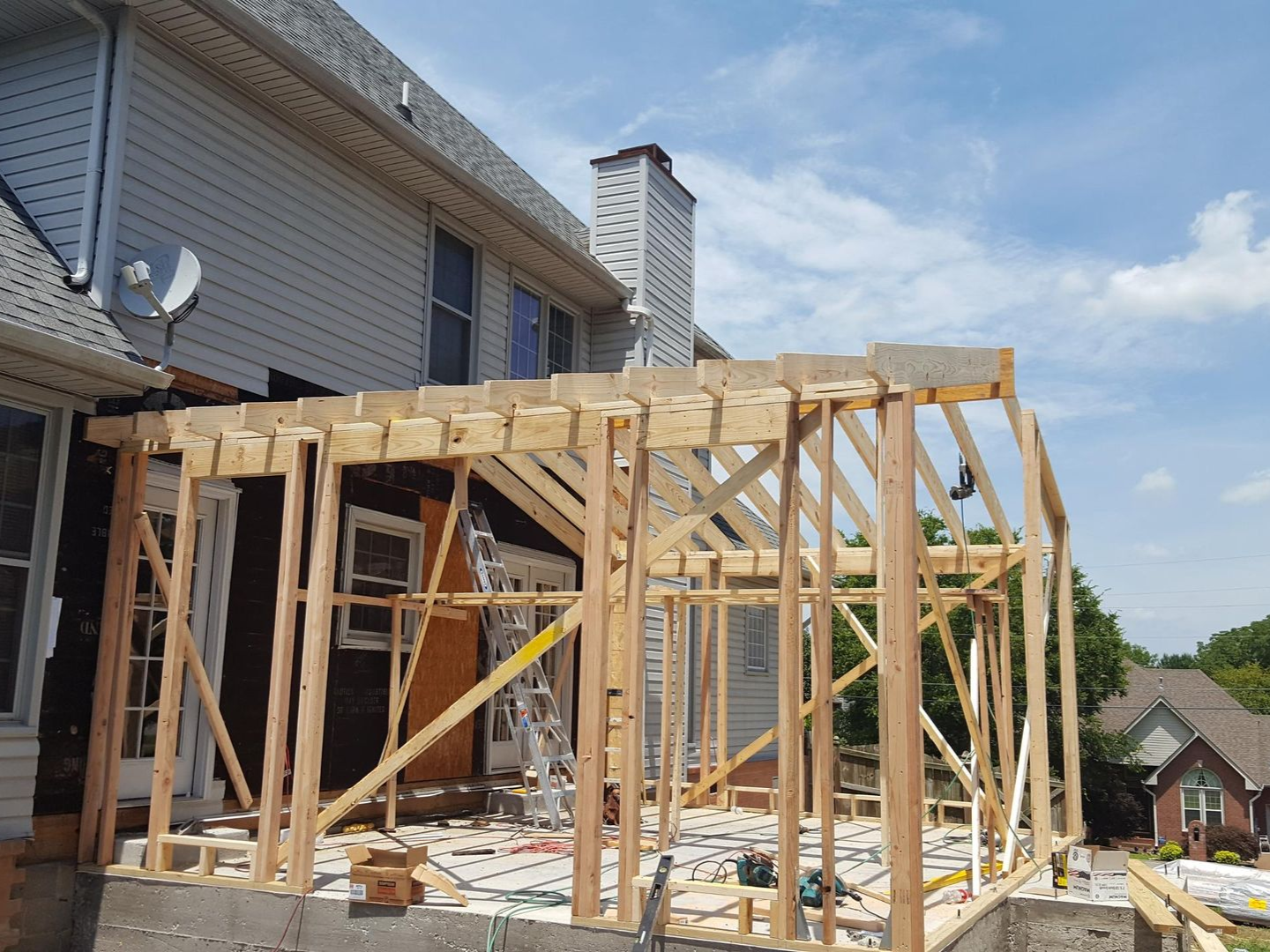 Wood frame of a sunroom addition attached to a two-story house under construction.