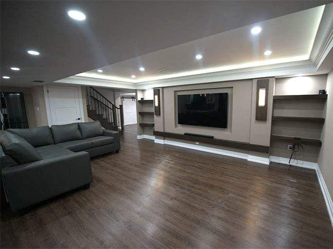 Finished basement with large TV, sectional sofa, built-in shelves, and dark wood floors.